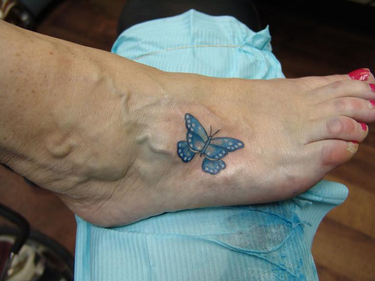 Colorful blue butterfly tattoo on the side of the foot