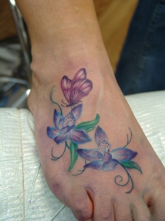 butterfly and flower tattoos on foot. Colorful feminine orchid flowers with a butterfly on the top of the foot.